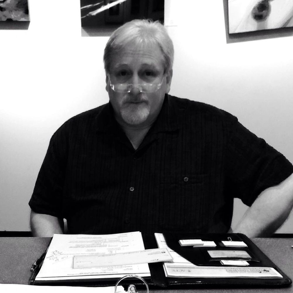 Man with glasses sitting at a desk with papers and folders.