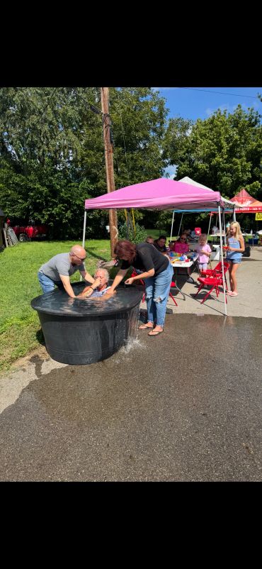 People assisting a child in a water tub at an outdoor event.