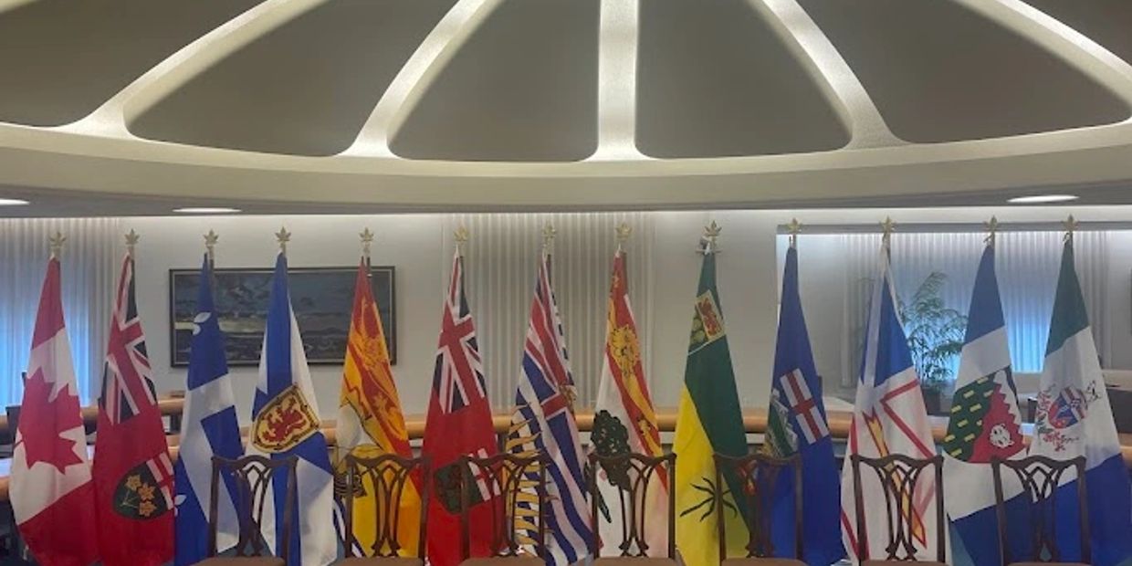 Row of Canadian provincial flags displayed indoors with chairs beneath.
