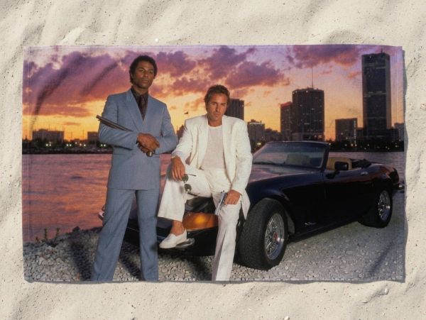 Two men in suits posing by a convertible car at sunset.