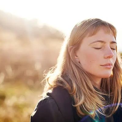 A woman with closed eyes enjoying sunlight outdoors.