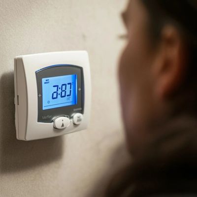 Person adjusting a digital thermostat on a wall.