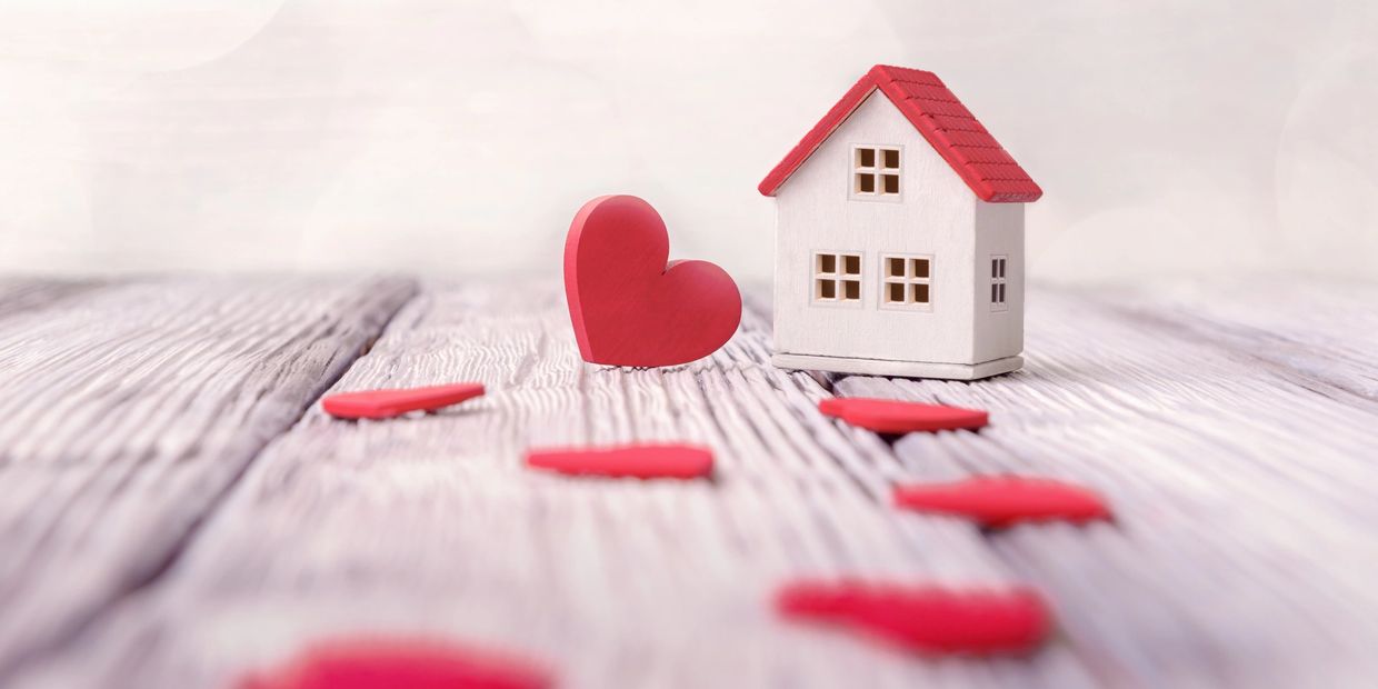 Miniature house with red hearts on wooden surface symbolizing love and home.