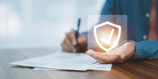 Person signing documents with a glowing shield checkmark symbolizing security.