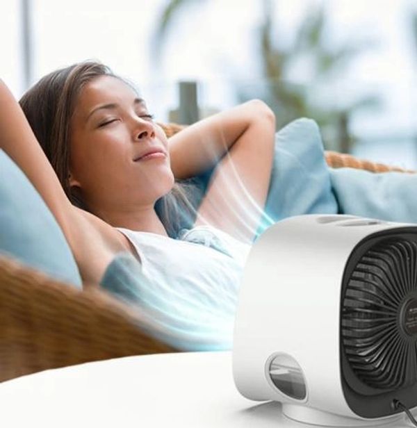 A woman relaxing with eyes closed near a small white fan.
