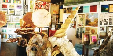 An eclectic gallery with wooden sculptures and framed paintings.