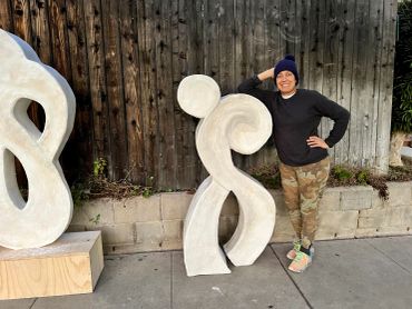 Person posing with abstract sculptures outdoors.