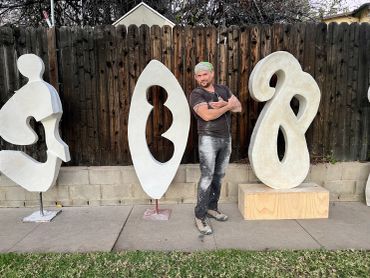 Man posing with abstract sculptures in a backyard.