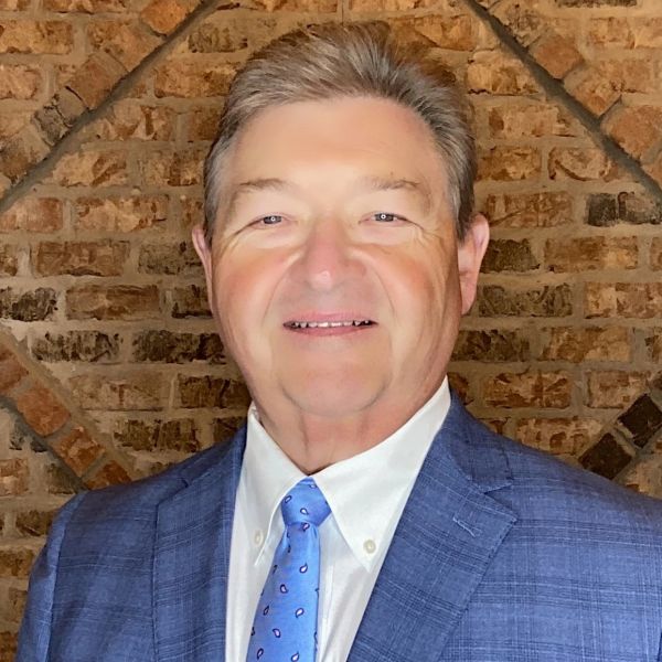 Smiling man in blue suit and tie against brick wall background.