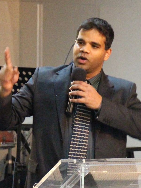 Man speaking passionately behind a transparent podium at a church or conference.