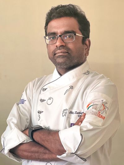 Confident chef in white uniform with folded arms.