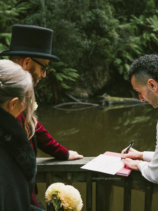 Two people watching another sign a document outdoors by a pond.