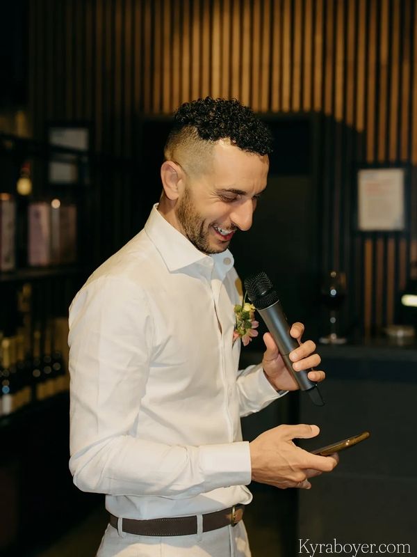 Man in white shirt holding microphone and phone, smiling.