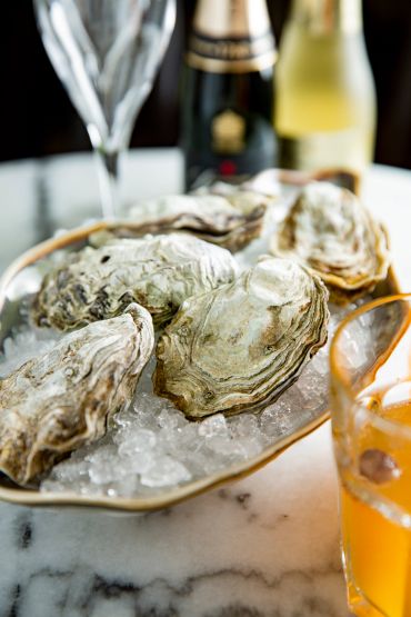 Oysters on ice with drinks in background.