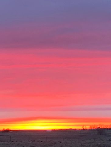 Vibrant sunset with hues of pink, orange, and purple over a flat landscape.