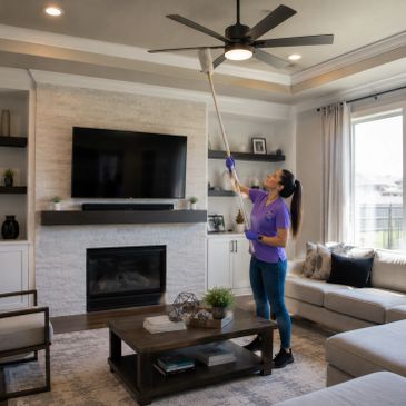 Woman cleaning ceiling fan with a vacuum extension in a living room.