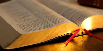 An open book with golden edges and two red ribbons.