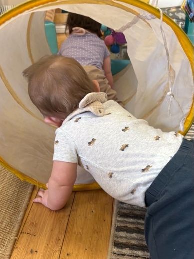 A toddler crawling into a play tunnel after another child.