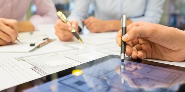 People collaborating on architectural plans using paper and a digital tablet.