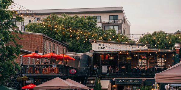 Crowded outdoor dining area with string lights and a modern building.in Fredericton