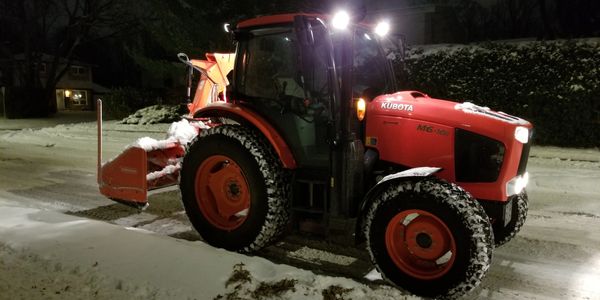 Red Kubota tractor clearing snow at night.