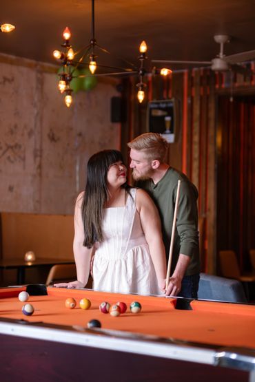 Couple sharing a tender moment by a pool table in a cozy setting.