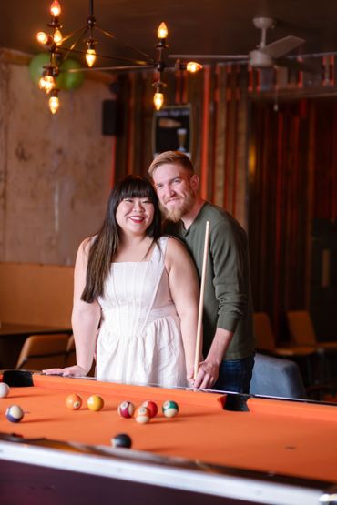 Couple smiling by a pool table in a warmly lit room.