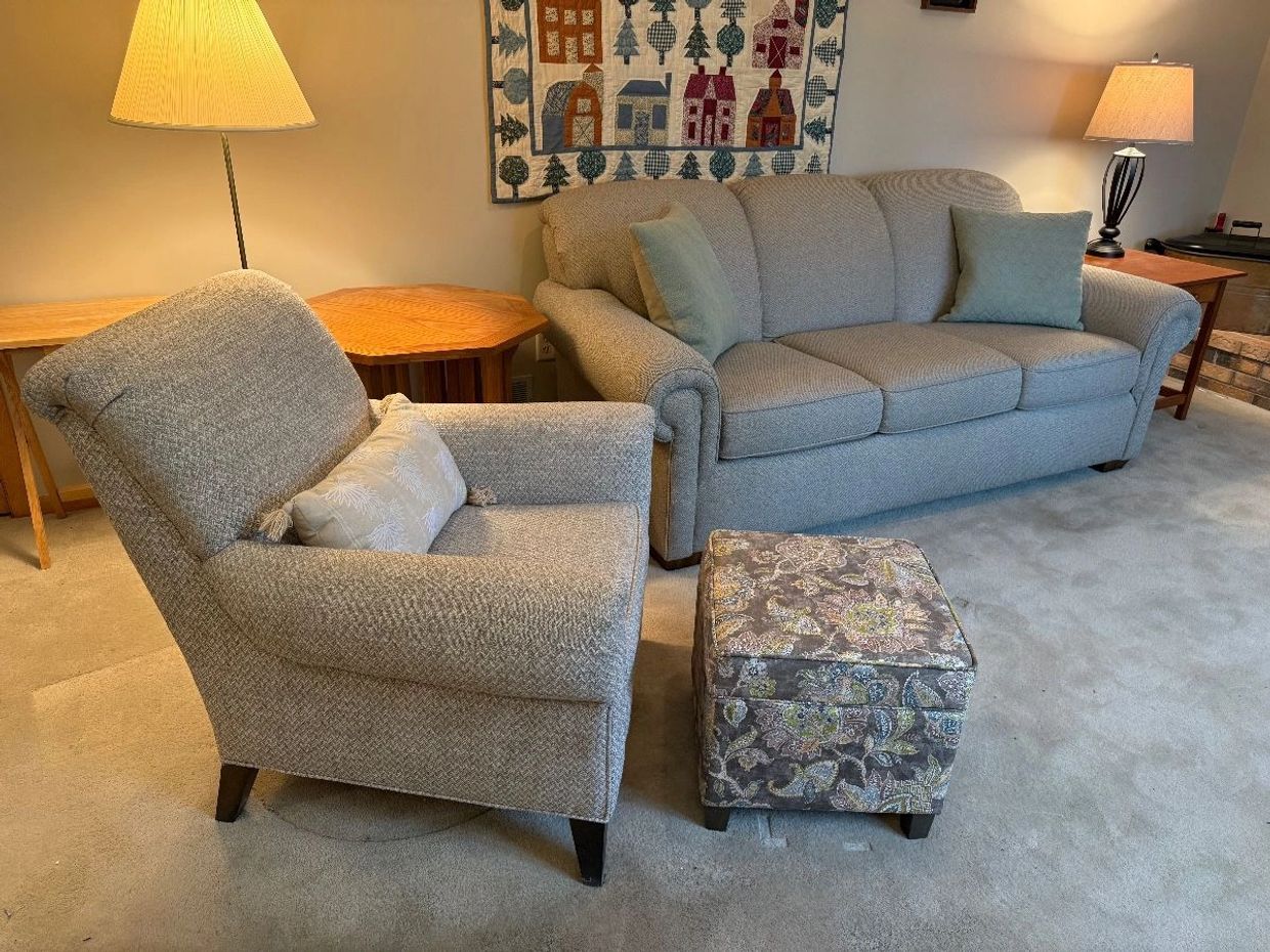 Cozy living room with beige sofa, armchair, patterned ottoman, and warm lighting.