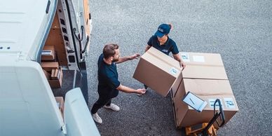Two men unloading large cardboard boxes from a delivery van outdoors.