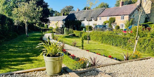 A sunny garden path with plants and charming cottages in the background.