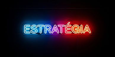 Neon sign spelling 'ESTRATÉGIA' in blue, purple, and red on a dark wall.