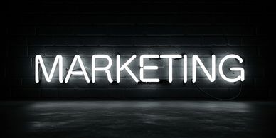 Bright white neon sign spelling "MARKETING" against a dark brick wall.
