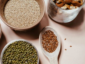 Bowls and a spoon with various seeds and grains on a light surface.
