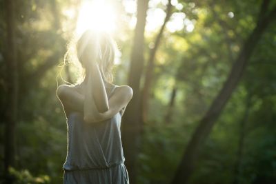 Woman standing in sunlight in a forest, partially obscured by bright light.