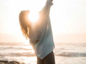 Person stretching by the beach at sunrise with sunlight glowing.