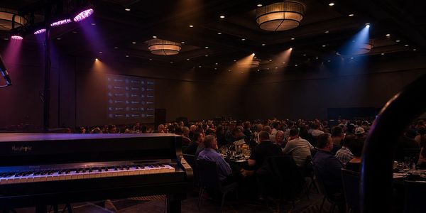Piano on stage with audience in a dimly lit event hall.