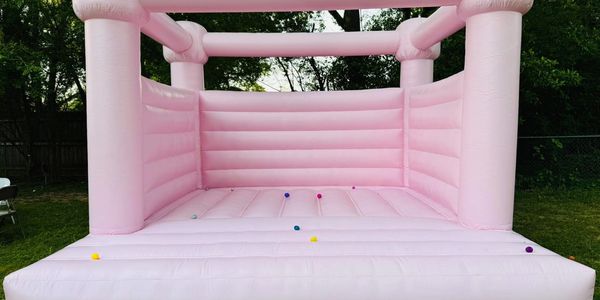Large pink inflatable bounce house outdoors with small colorful balls inside.