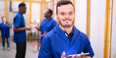 Smiling healthcare worker with tablet in a busy medical setting.