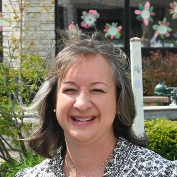 Smiling woman outdoors with decorative flower window art behind her.