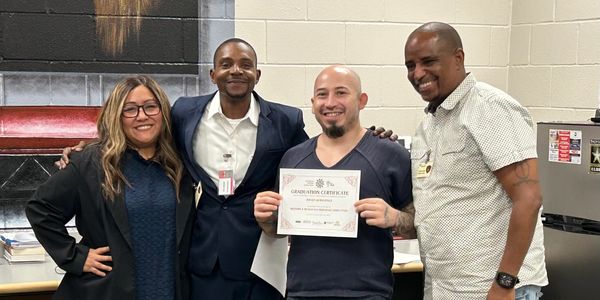 Four smiling colleagues, one holding a certificate, celebrating achievement.