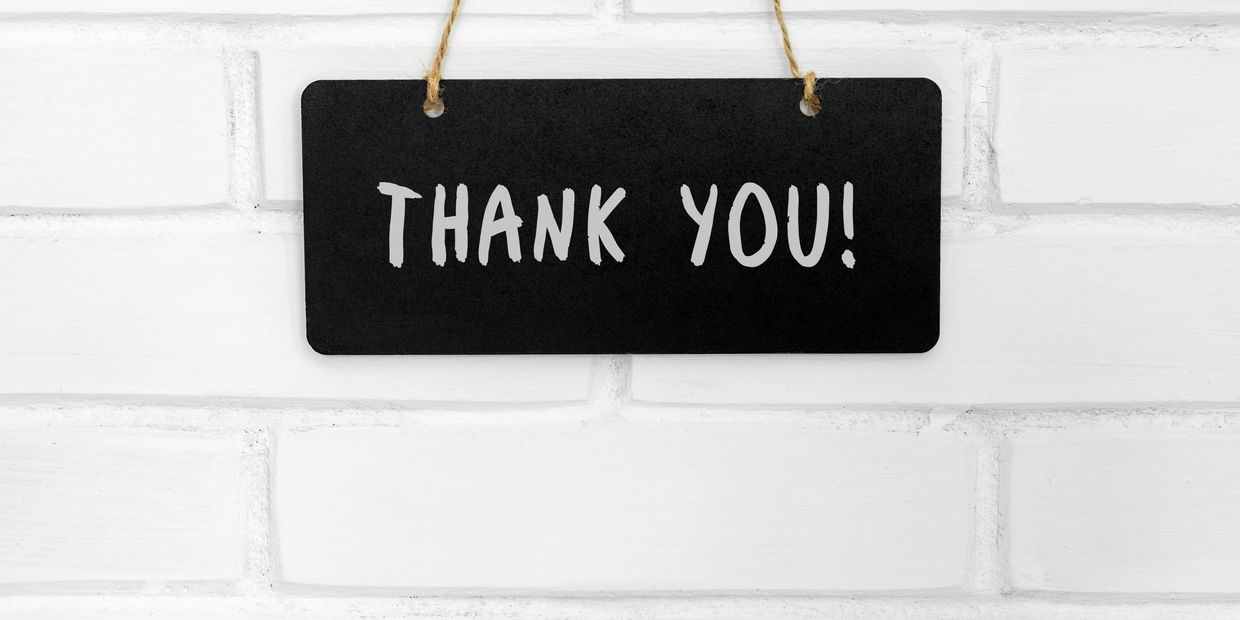 Black sign with white text saying "THANK YOU!" hanging on a white brick wall.