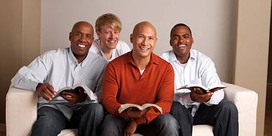 Four men happily sitting on a couch, reading books together.