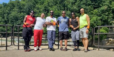 Six men posing outdoors near a river with greenery in the background.