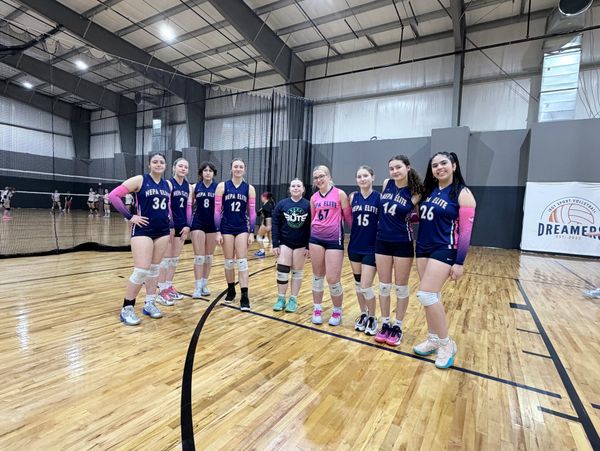 Youth volleyball team posing in gym, wearing matching uniforms and knee pads.