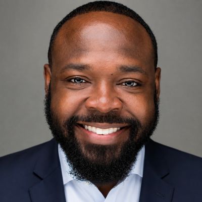 Smiling man with beard in suit against gray background.