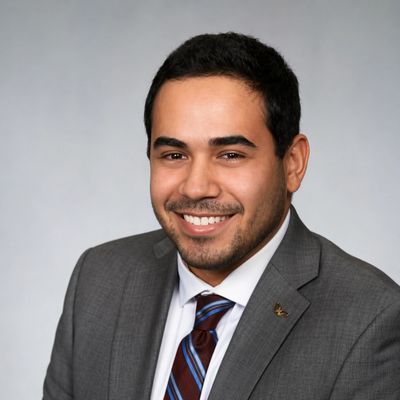 Smiling man in a grey suit and striped tie against a neutral background.