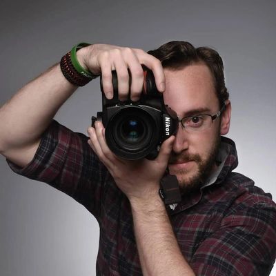 Man with glasses holding a Nikon camera up to his face.