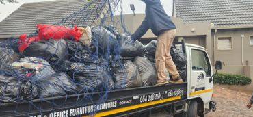 A person arranging bags on a loaded removal truck outside a house.