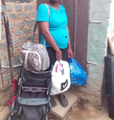 Pregnant woman standing with bags and a stroller outside a house.