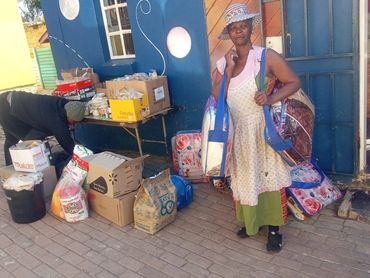 Woman carrying bags of groceries outside a building with supplies stacked nearby.